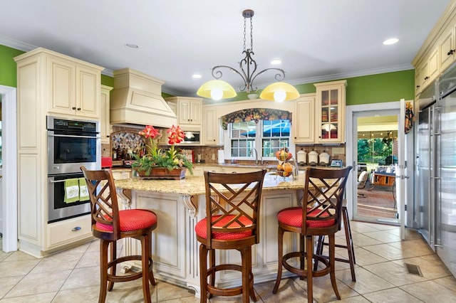 kitchen with decorative light fixtures, premium range hood, cream cabinetry, and stainless steel double oven