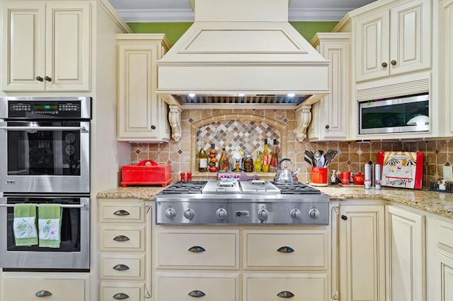 kitchen featuring premium range hood, cream cabinets, decorative backsplash, and stainless steel appliances