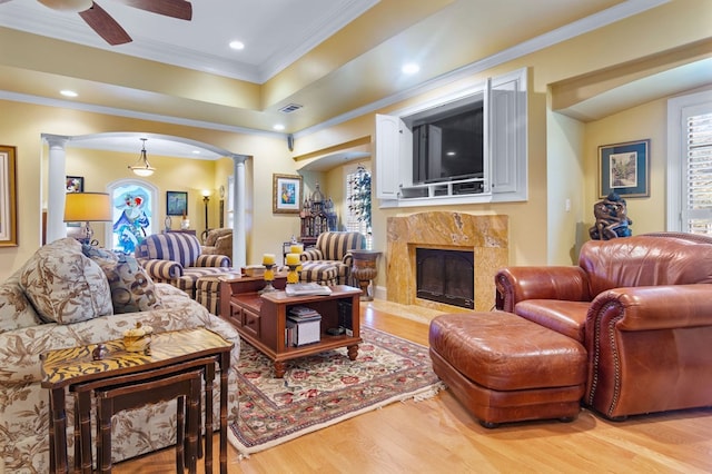 living room featuring hardwood / wood-style floors, a high end fireplace, ceiling fan, ornamental molding, and decorative columns