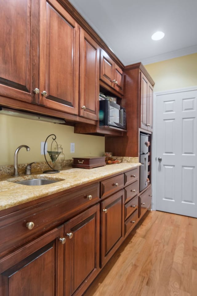 kitchen featuring sink, light stone counters, light wood-type flooring, and crown molding