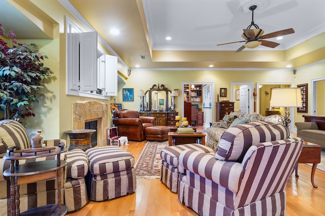 living room with a fireplace, light hardwood / wood-style flooring, a raised ceiling, and crown molding