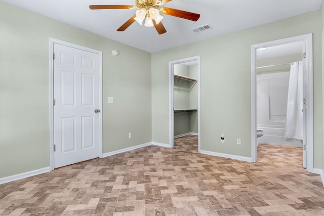 unfurnished bedroom featuring ceiling fan, ensuite bathroom, and a spacious closet