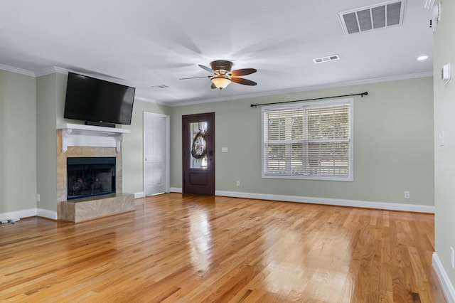 unfurnished living room with crown molding, a tiled fireplace, light wood-type flooring, and ceiling fan