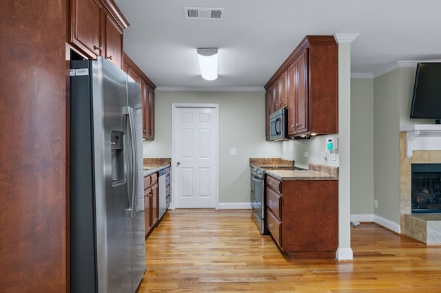 kitchen featuring crown molding, a tile fireplace, light hardwood / wood-style floors, and appliances with stainless steel finishes