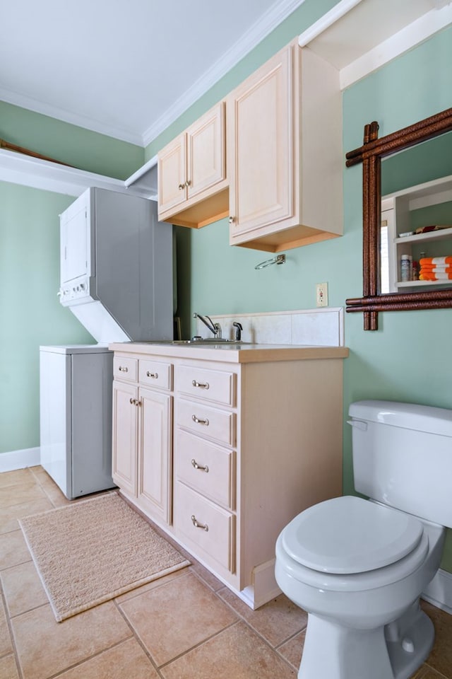 bathroom featuring tile patterned flooring, toilet, baseboards, ornamental molding, and stacked washing maching and dryer