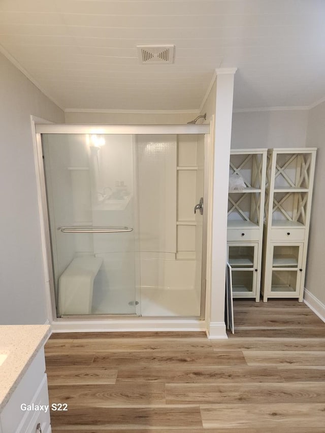 bathroom featuring hardwood / wood-style flooring, walk in shower, vanity, and ornamental molding