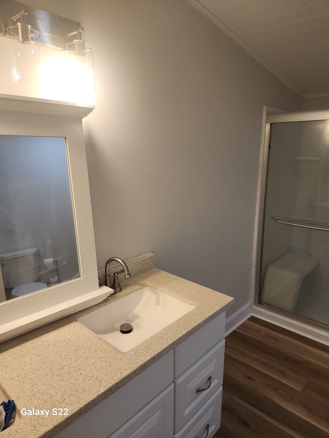 bathroom featuring wood-type flooring, an enclosed shower, toilet, vanity, and ornamental molding