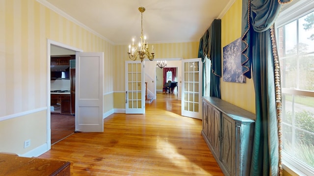 unfurnished dining area featuring crown molding, hardwood / wood-style flooring, a chandelier, and french doors