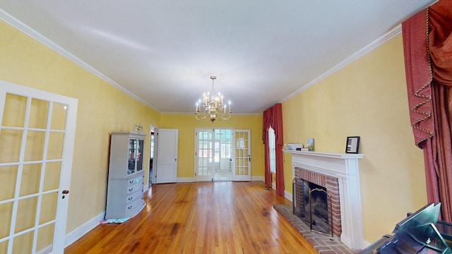 unfurnished living room featuring a brick fireplace, wood-type flooring, ornamental molding, and a notable chandelier