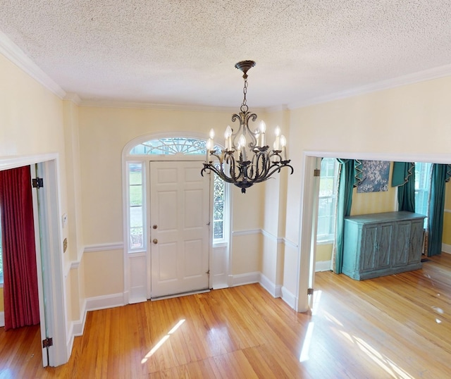 foyer entrance with hardwood / wood-style floors, ornamental molding, a notable chandelier, and a textured ceiling