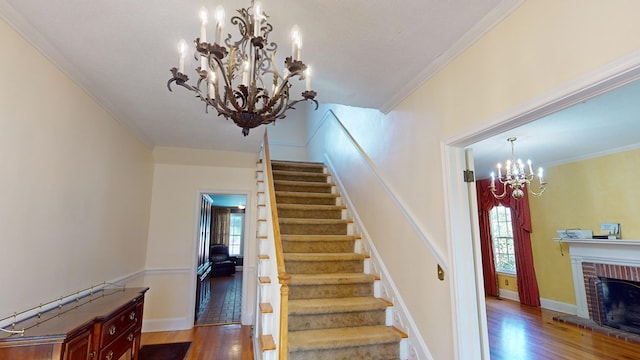 staircase with a notable chandelier, hardwood / wood-style floors, a textured ceiling, a brick fireplace, and ornamental molding