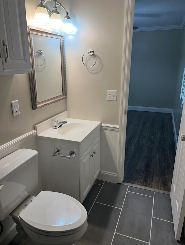 half bath with a wainscoted wall, crown molding, toilet, vanity, and tile patterned flooring