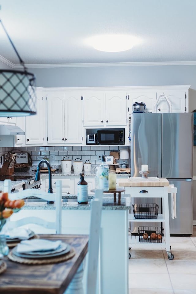 kitchen with light stone counters, backsplash, white cabinetry, and stainless steel refrigerator