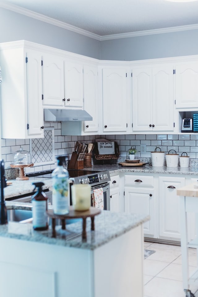 kitchen featuring white cabinets, crown molding, decorative backsplash, and light tile patterned flooring