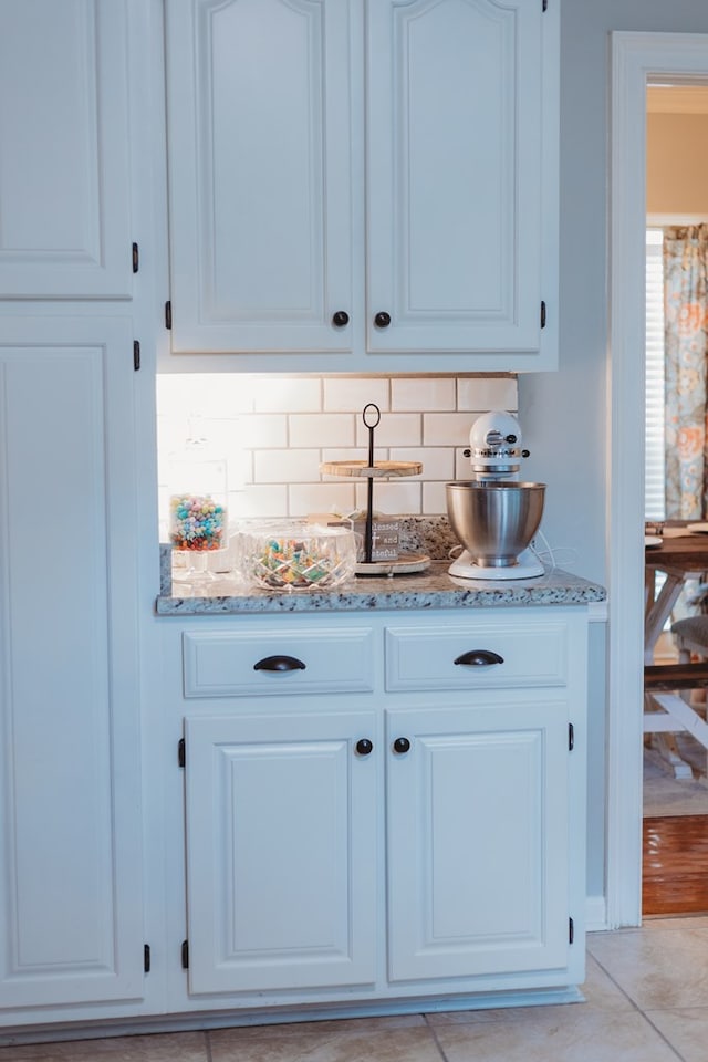 bar with light tile patterned floors, light stone countertops, backsplash, and white cabinets