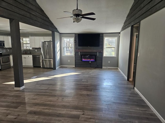 unfurnished living room with a large fireplace, baseboards, dark wood-style floors, vaulted ceiling, and a sink