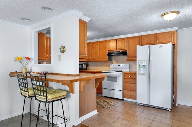 kitchen with white appliances, light tile patterned floors, crown molding, under cabinet range hood, and a kitchen bar