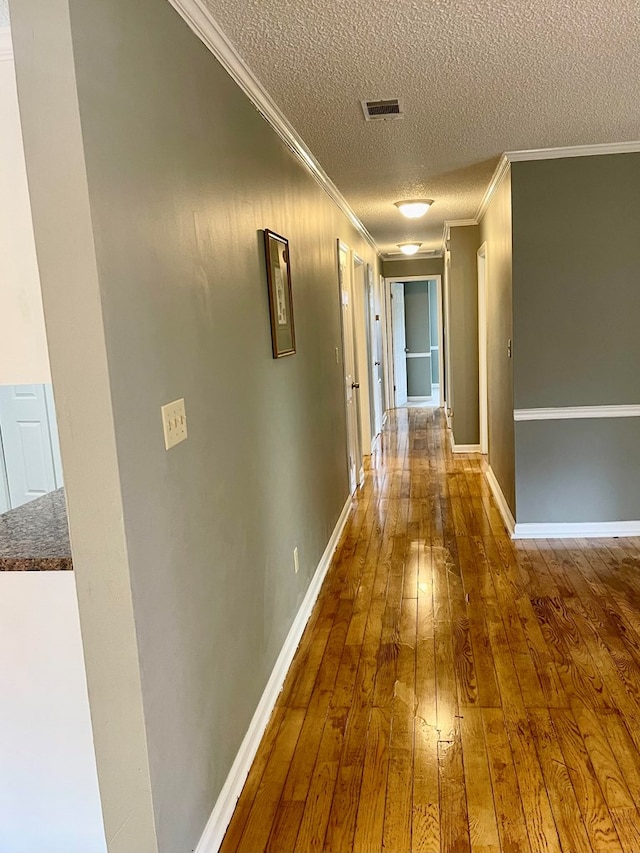 hallway featuring wood-type flooring, a textured ceiling, and ornamental molding