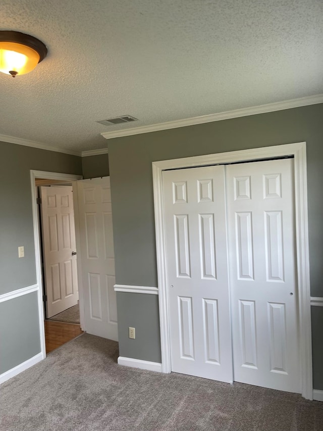 unfurnished bedroom featuring a textured ceiling, carpet floors, a closet, and ornamental molding