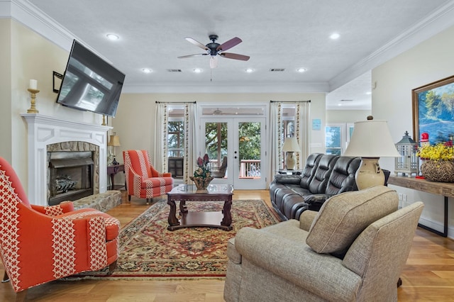 living room featuring a stone fireplace, a textured ceiling, french doors, ornamental molding, and light hardwood / wood-style flooring