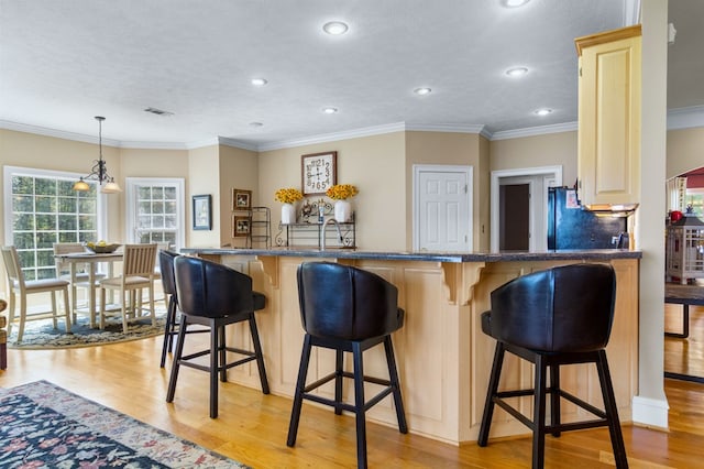 kitchen with kitchen peninsula, light wood-type flooring, a breakfast bar area, and hanging light fixtures