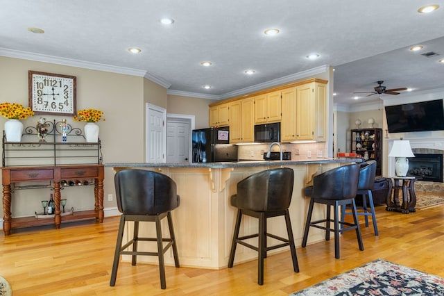 kitchen with black appliances, light brown cabinets, light wood-type flooring, a breakfast bar, and crown molding