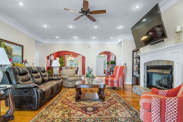 living room featuring ceiling fan with notable chandelier, light hardwood / wood-style flooring, crown molding, and a stone fireplace