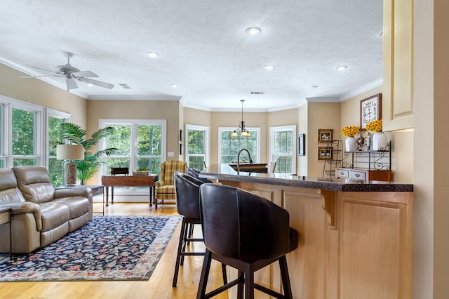 kitchen with a kitchen breakfast bar, decorative light fixtures, a textured ceiling, ornamental molding, and light hardwood / wood-style floors