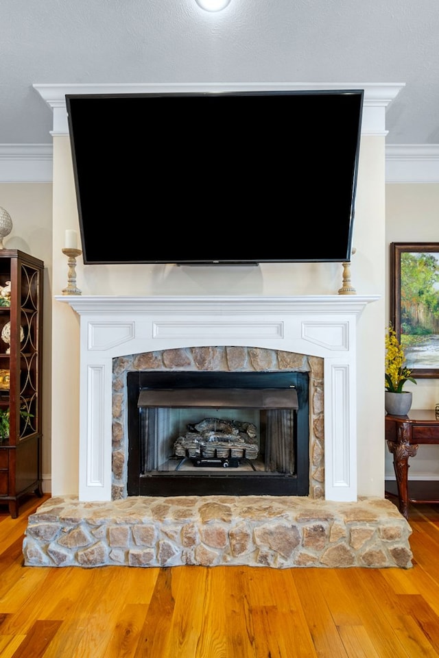 interior details with hardwood / wood-style flooring, ornamental molding, and a stone fireplace