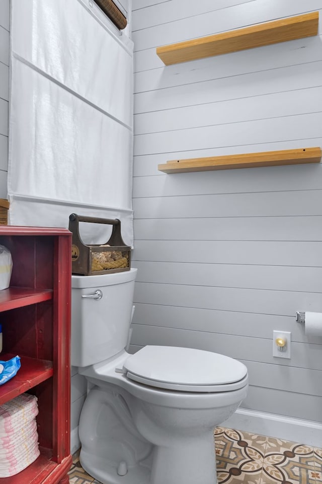 bathroom with toilet, wood walls, and tile patterned flooring