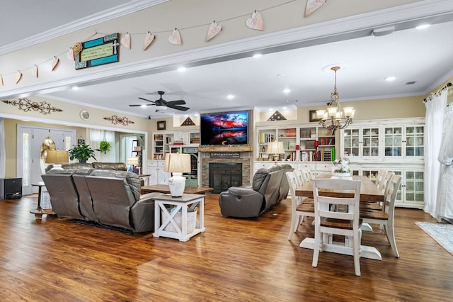 living room with ceiling fan with notable chandelier, wood finished floors, a fireplace, and ornamental molding
