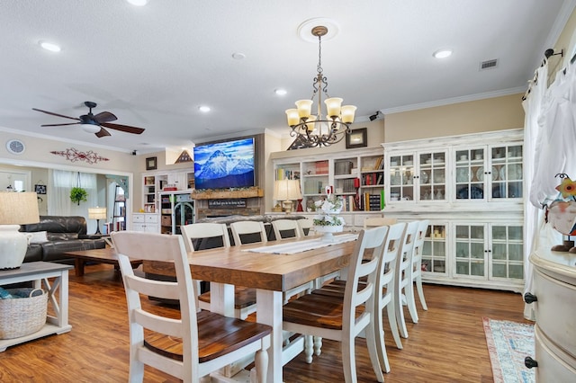 dining space with wood finished floors, visible vents, crown molding, and ceiling fan with notable chandelier