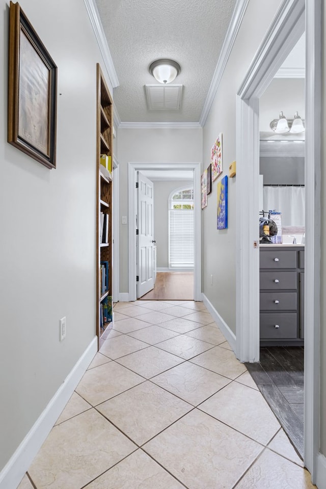 hallway featuring a textured ceiling, baseboards, visible vents, crown molding, and light tile patterned floors