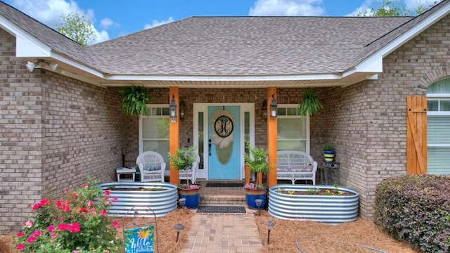 entrance to property featuring covered porch, brick siding, and roof with shingles