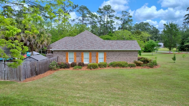 view of side of home with brick siding, roof with shingles, fence, and a yard
