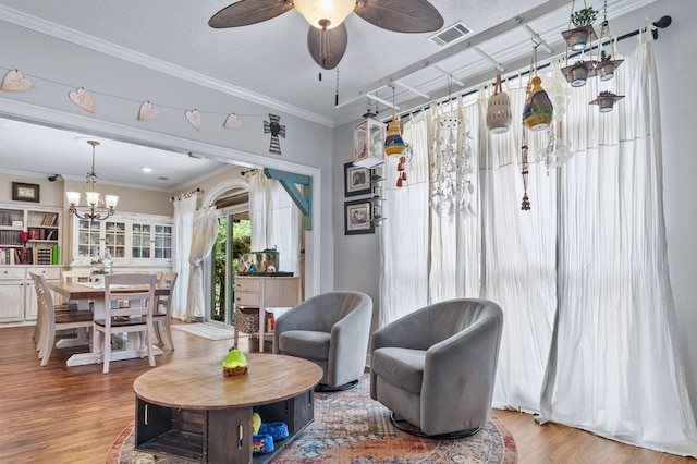 sitting room with wood finished floors, visible vents, ornamental molding, and ceiling fan with notable chandelier