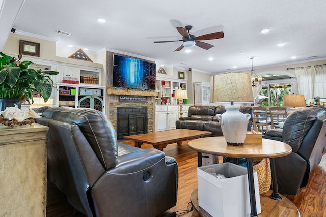 living area with wood finished floors, ceiling fan, a fireplace, ornamental molding, and visible vents