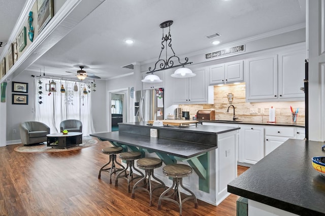 kitchen with dark countertops, tasteful backsplash, stainless steel refrigerator with ice dispenser, white cabinetry, and a kitchen island