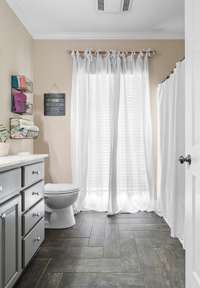 bathroom with toilet, crown molding, vanity, and visible vents
