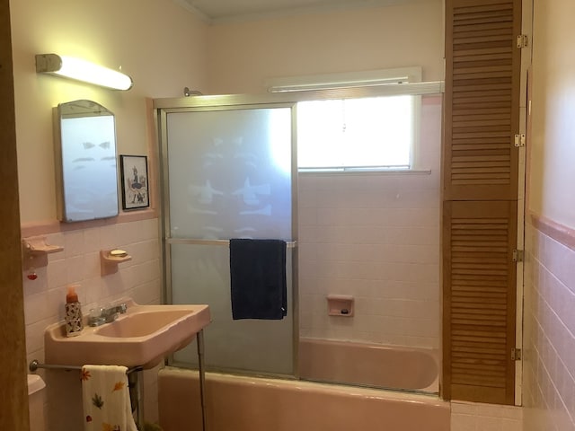 full bathroom with a wainscoted wall, bath / shower combo with glass door, and tile walls