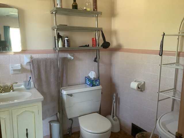 half bathroom featuring toilet, wainscoting, tile walls, and vanity