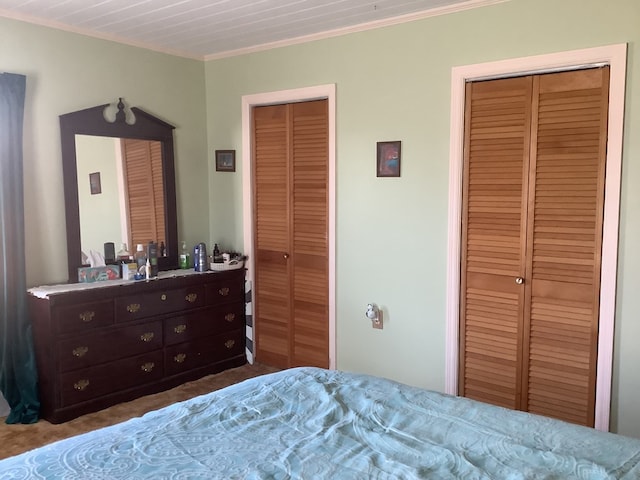 carpeted bedroom with ornamental molding and two closets