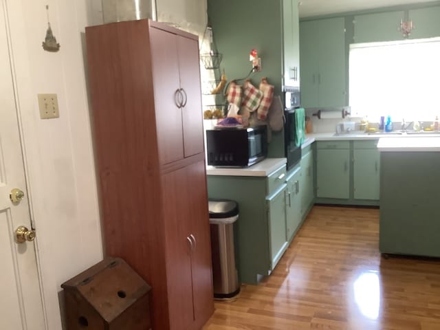 kitchen with black microwave, a sink, light wood-style floors, green cabinets, and light countertops