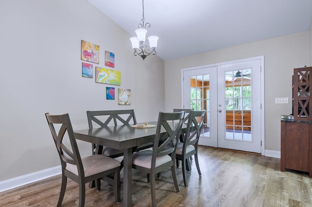 dining area featuring lofted ceiling, hardwood / wood-style floors, a notable chandelier, and french doors