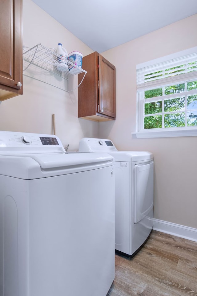 laundry area featuring cabinet space, baseboards, separate washer and dryer, and light wood-style floors