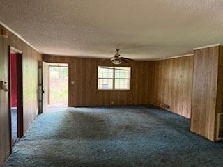 unfurnished room featuring dark colored carpet, wood walls, a textured ceiling, and a ceiling fan