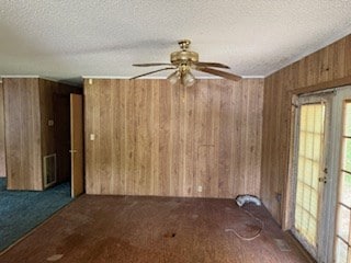 carpeted spare room with wooden walls, ceiling fan, a textured ceiling, and visible vents