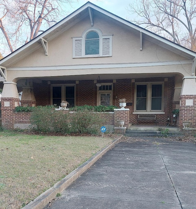 view of front of property featuring a front yard, covered porch, brick siding, and stucco siding