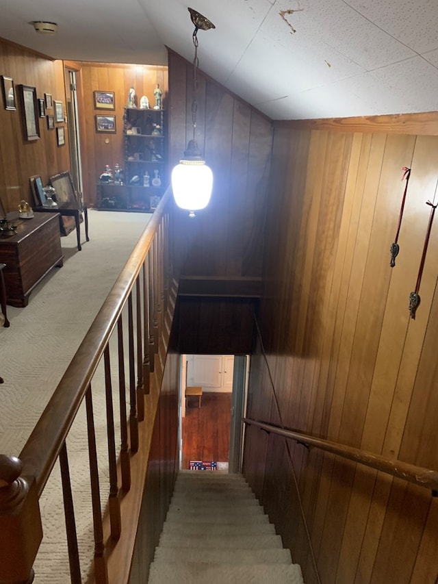 stairway featuring vaulted ceiling, carpet floors, and wooden walls