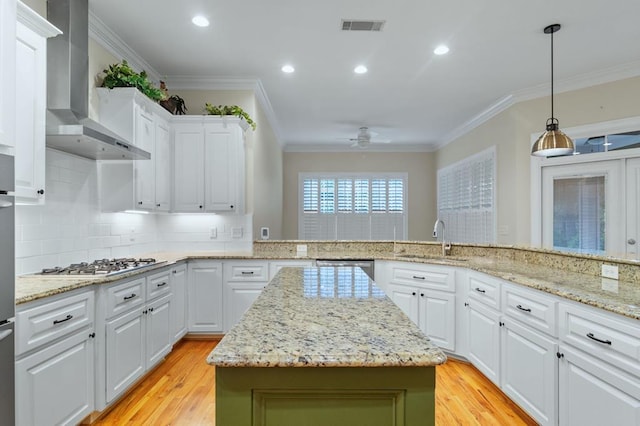 kitchen featuring a center island, wall chimney exhaust hood, white cabinetry, stainless steel appliances, and sink